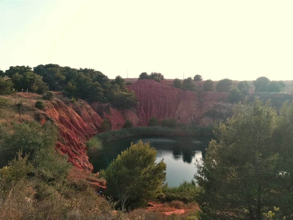 Vista sulla ex cava di Bauxite di Otranto con il contrasto tra il rosso del terreno, il verde degli alberi e il blu dell'acqua del lago, Otranto, Puglia