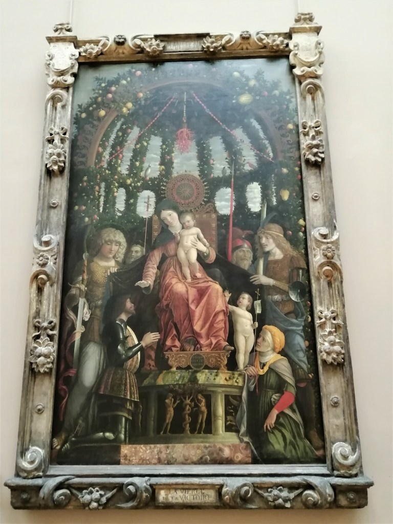 Opera di Mantegna esposta al Louvre che raffigura la "Madonna della Vittoria", oltre ai Santi si può vedere Francesco Gonzaga che aspetta la benedizione