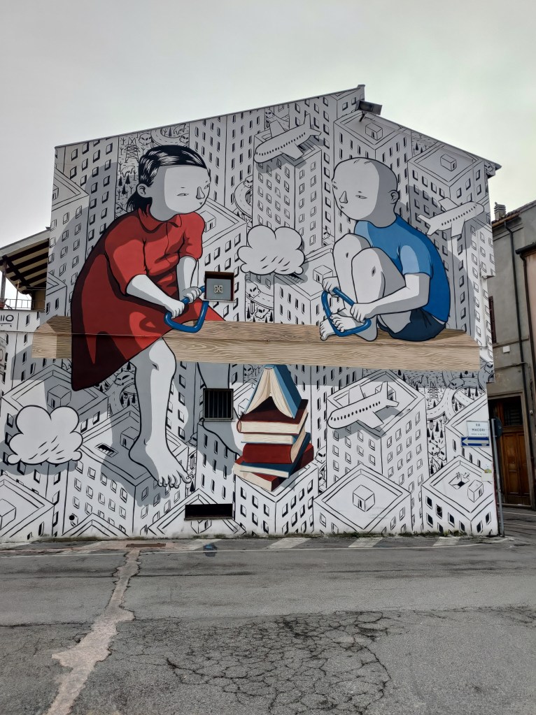 Il murales di Millo intitolato "Dignità" in Piazza del Carmine a Forlì con rappresentati 2 bambini (1 maschio e 1 femmina) con libri e giocattoli